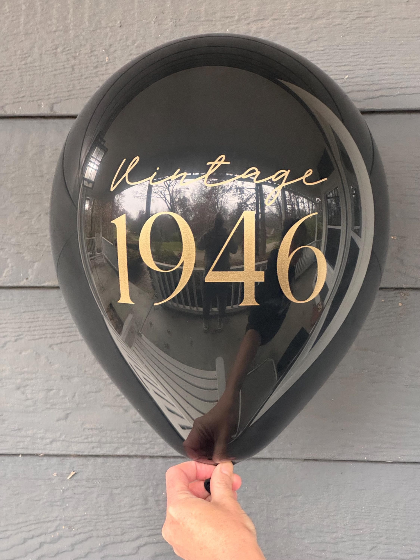 Black latex balloon with 'Vintage 1946' text held against a wooden surface.