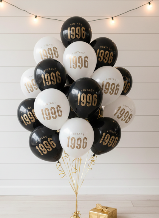 Bouquet of balloons with '1996' printed on them against a white wooden wall.