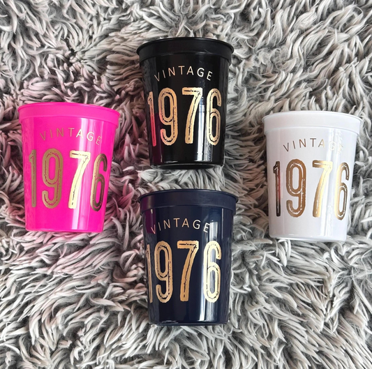 Four 'Vintage 1976' cups in different colors on a textured surface.