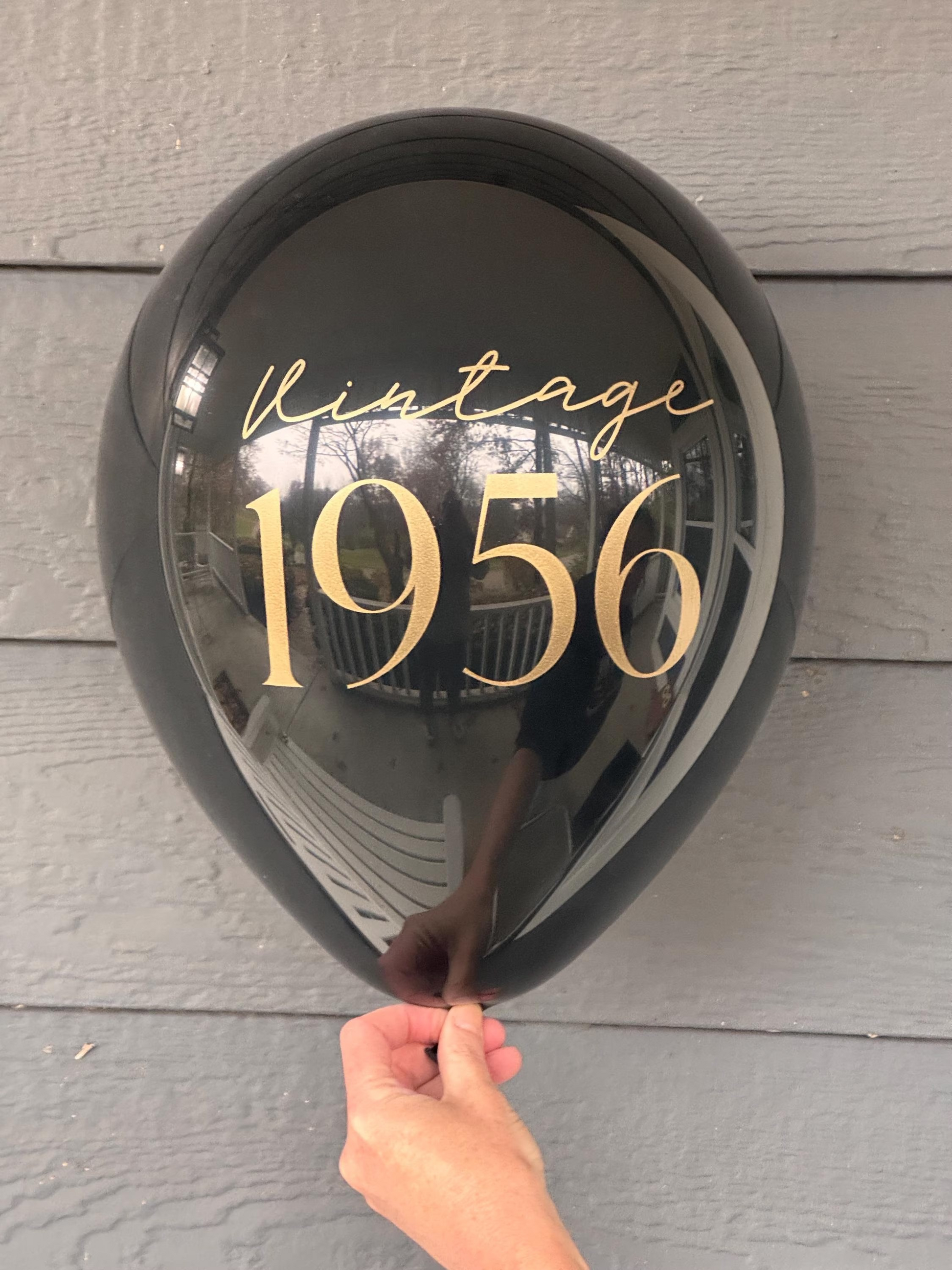 Black balloon with 'Vintage 1956' text held by a hand against a wooden surface