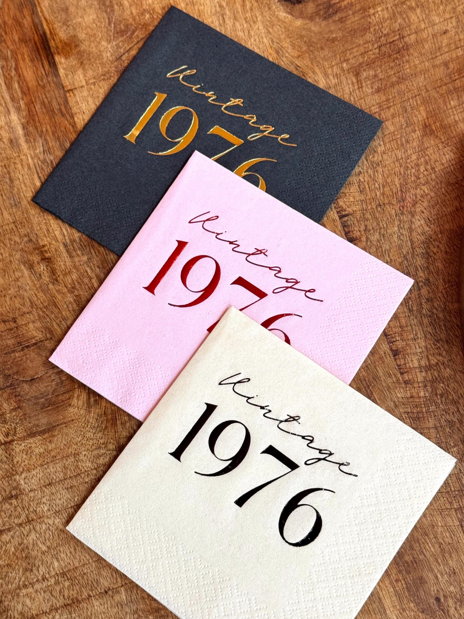 Three napkins with 'Vintage 1976' text on a wooden surface