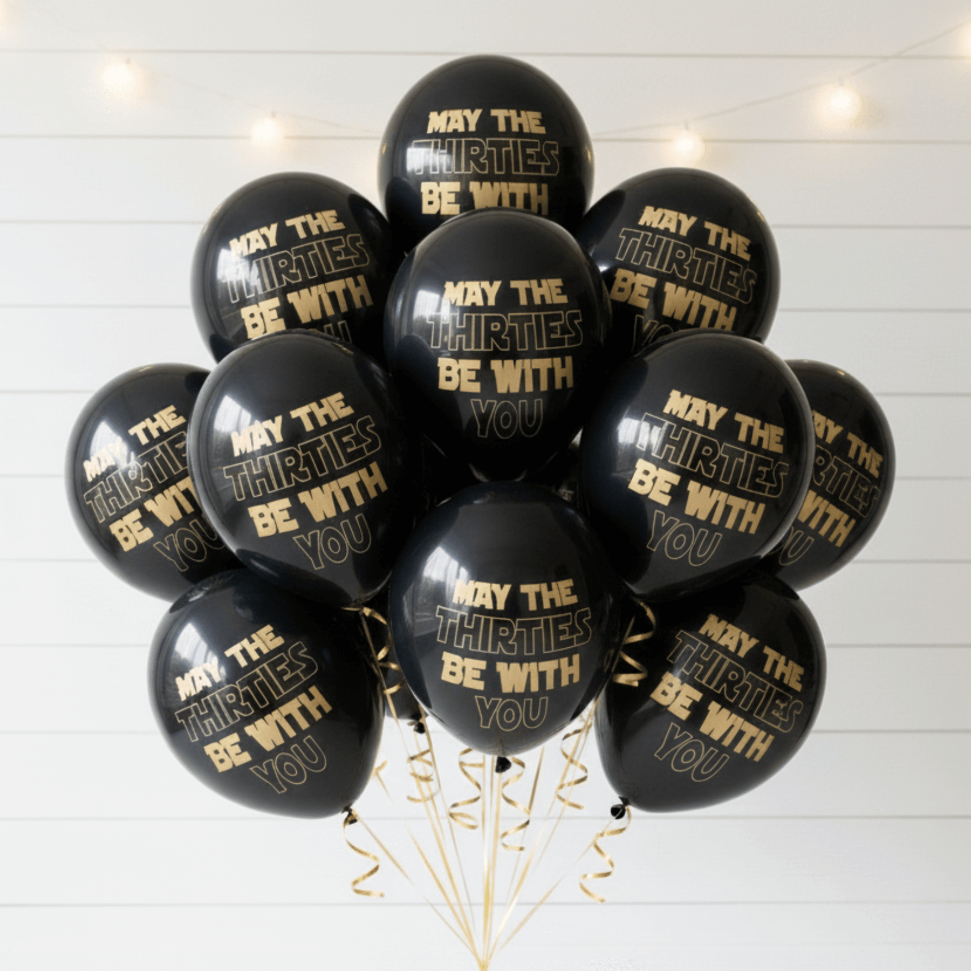 30th Birthday Balloons Black with gold text 'May the Thirties be with you' on a white wooden background