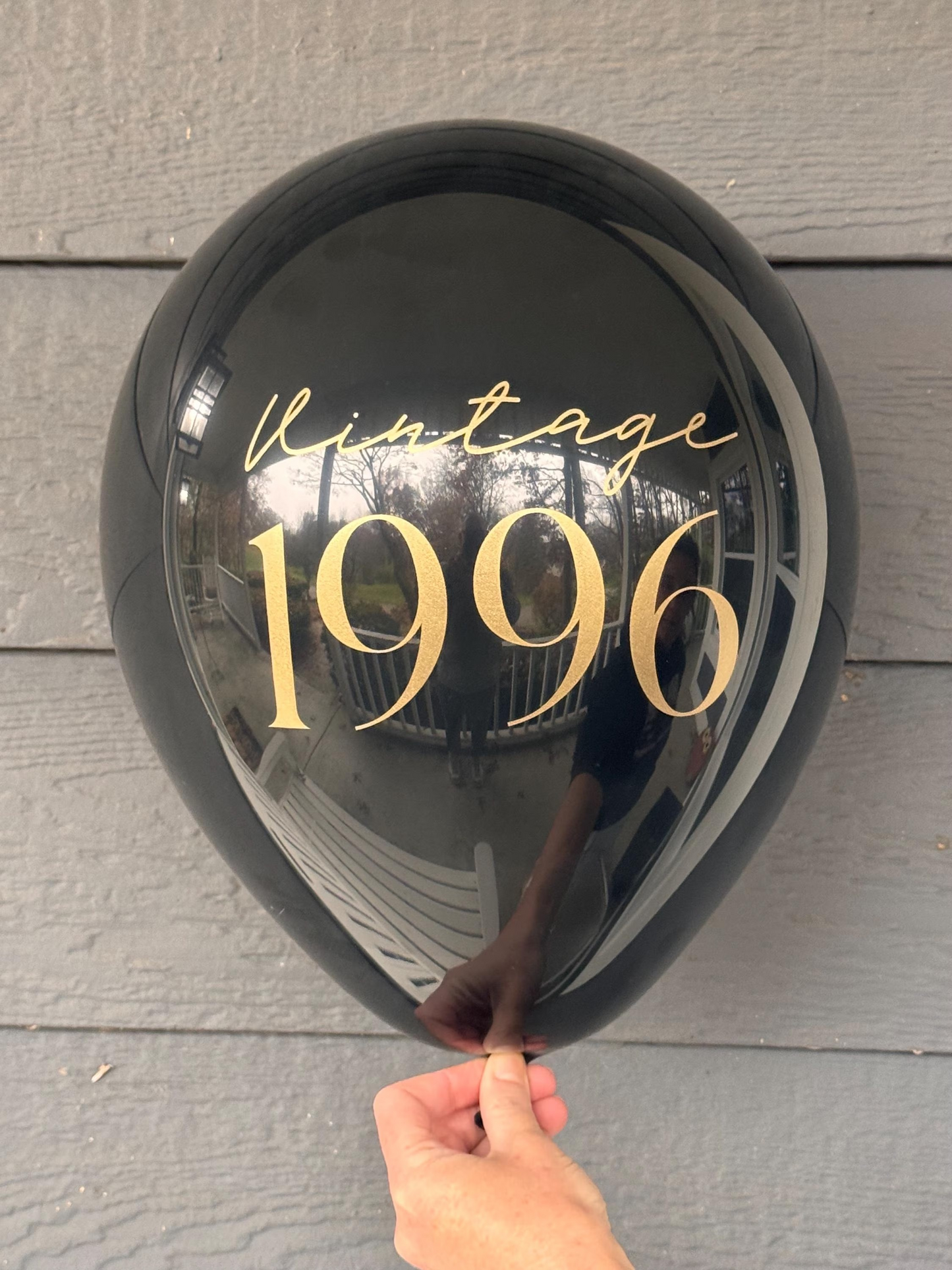 Black balloon with 'Vintage 1996' text held against a wooden surface