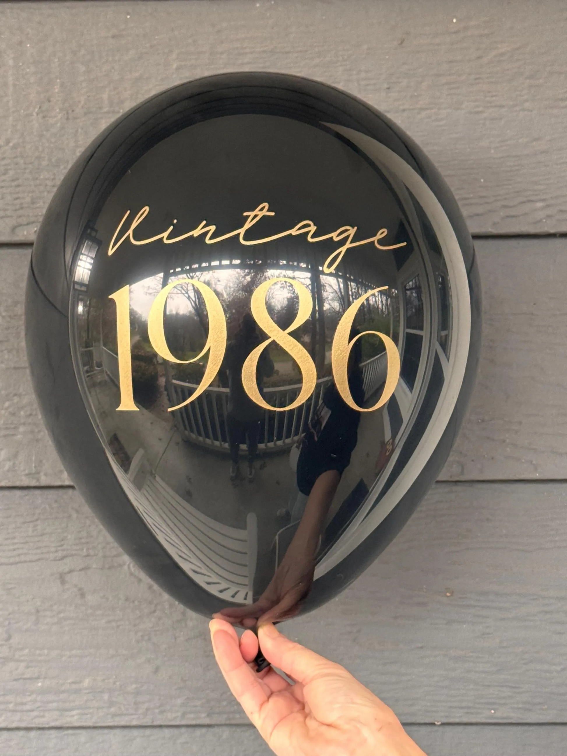 Round black latex balloon with 'Vintage 1986' text held by a hand on a wooden surface