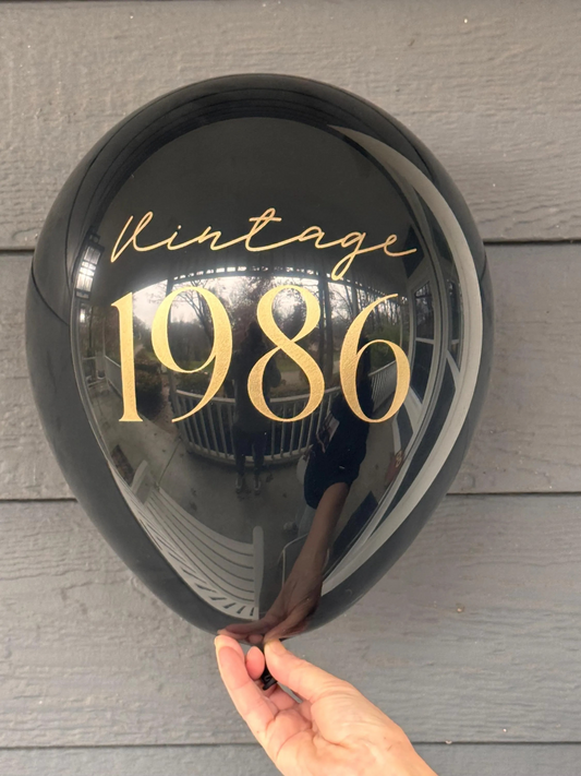 Round black latex balloon with 'Vintage 1986' text held by a hand on a wooden surface