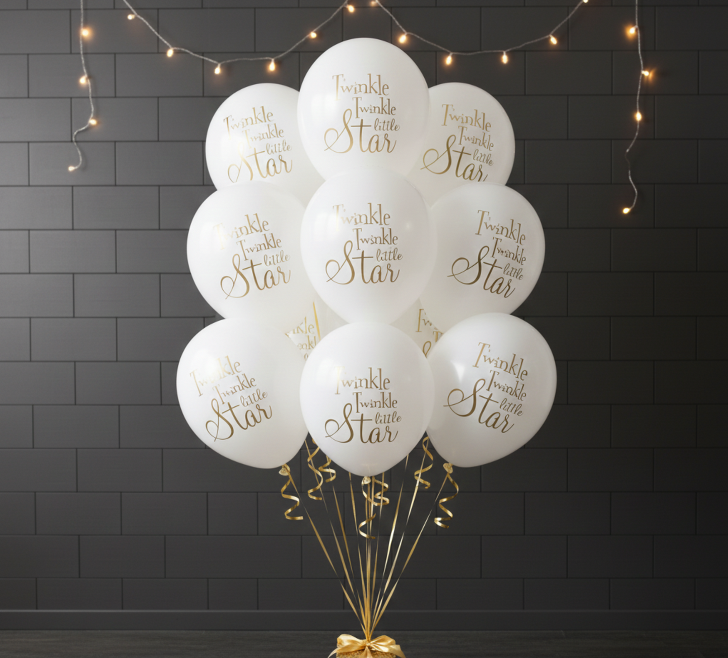 White balloons with gold text 'Twinkle twinkle little star' on a dark brick wall background.