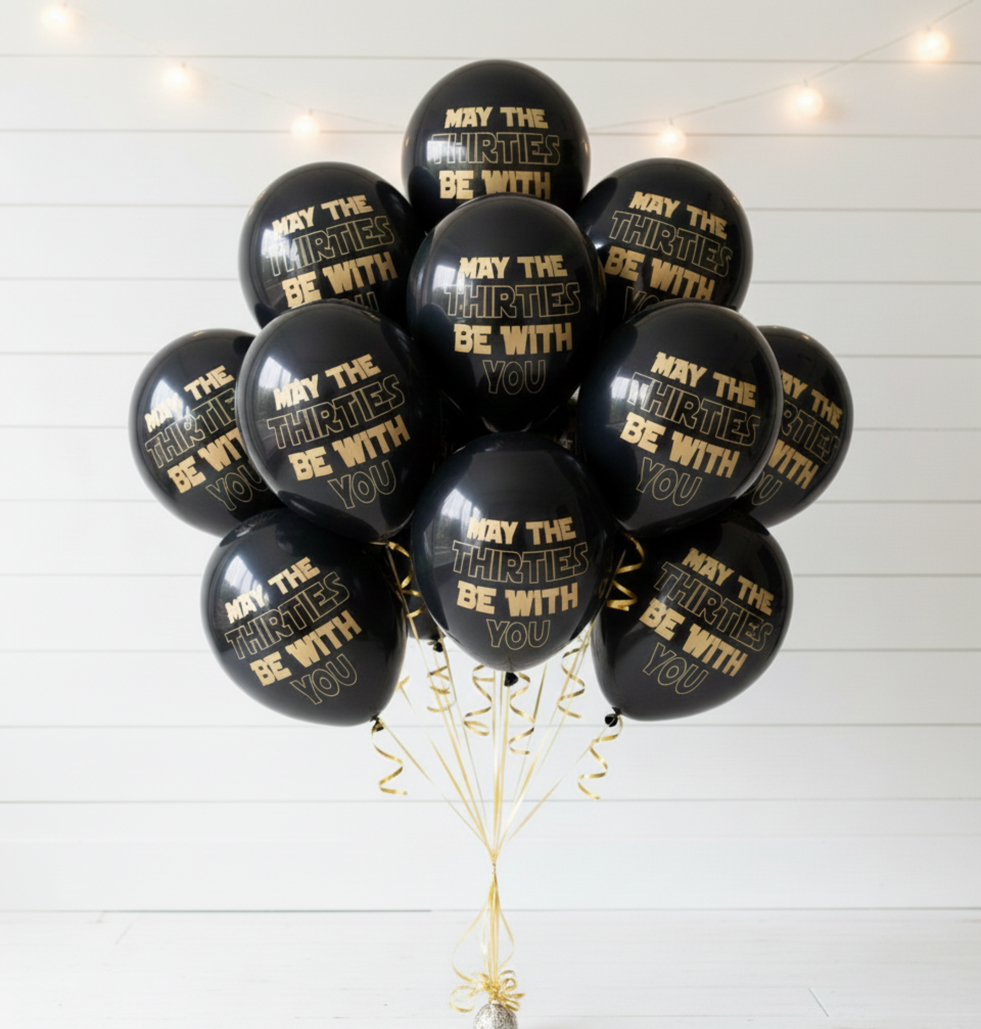 Black balloons with gold text 'May the Thirties be with you' on a white wooden background