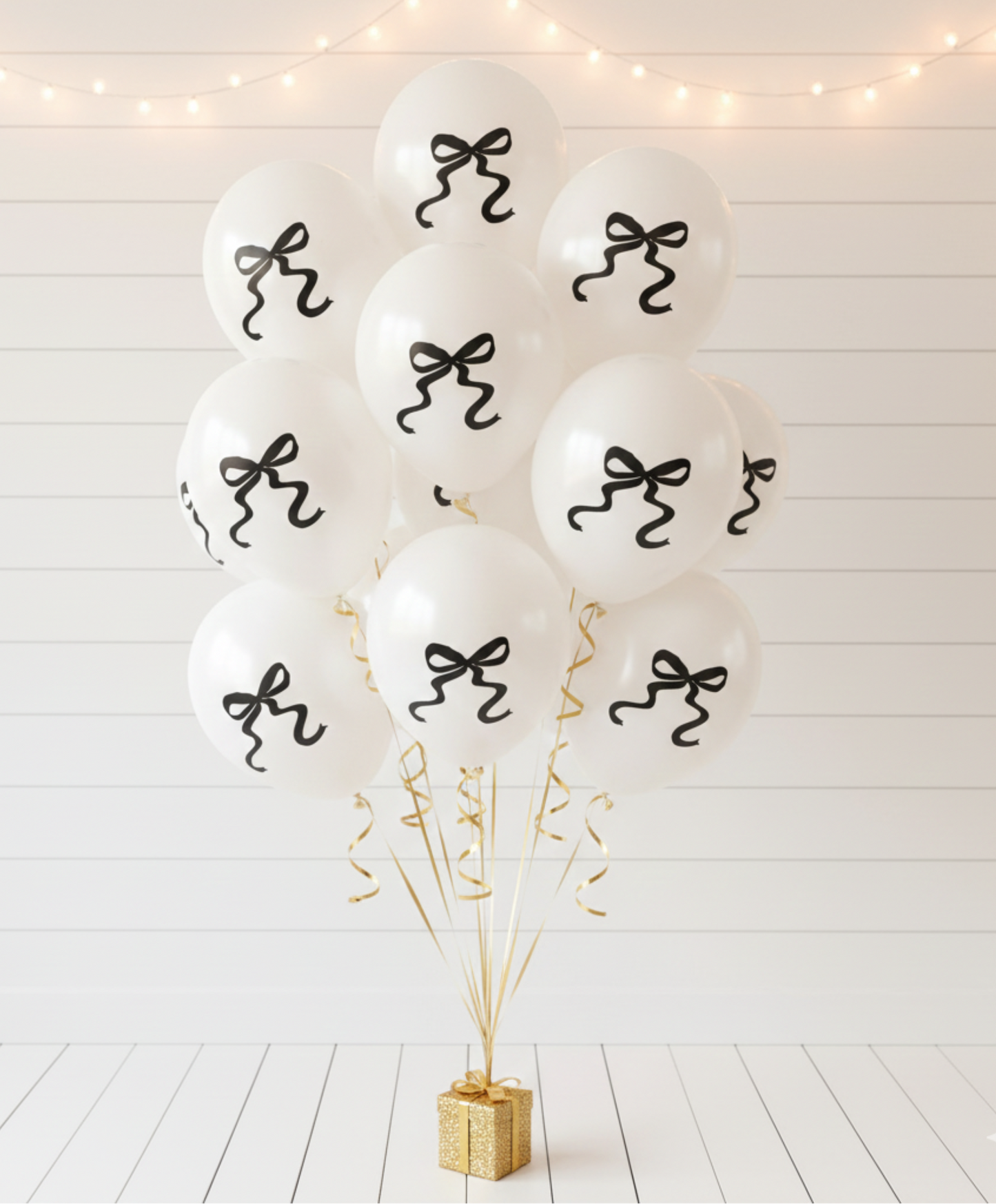 White balloons with black ribbons on a white wooden floor with decorative lights.