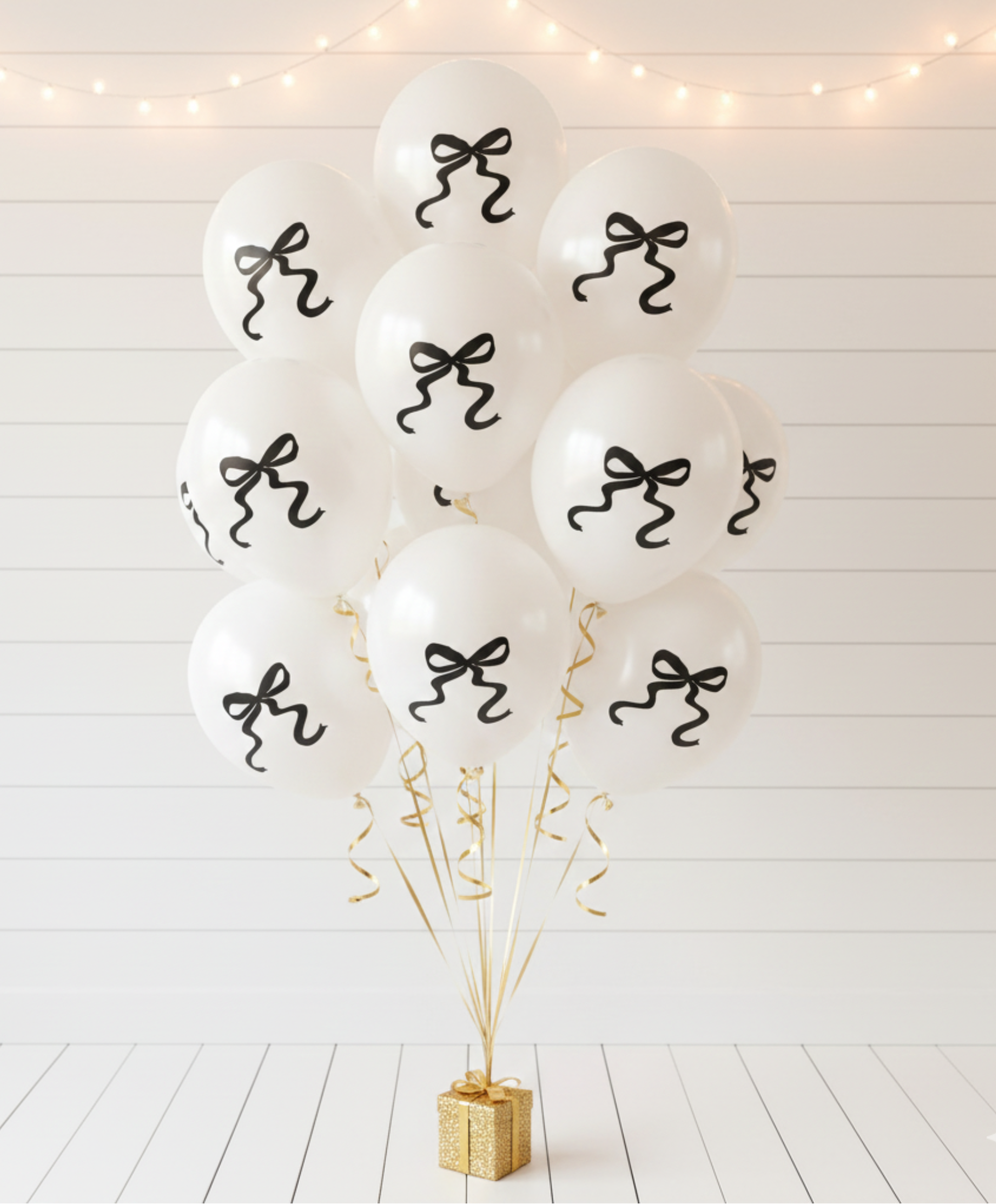 White balloons with black ribbons on a white wooden floor with decorative lights.