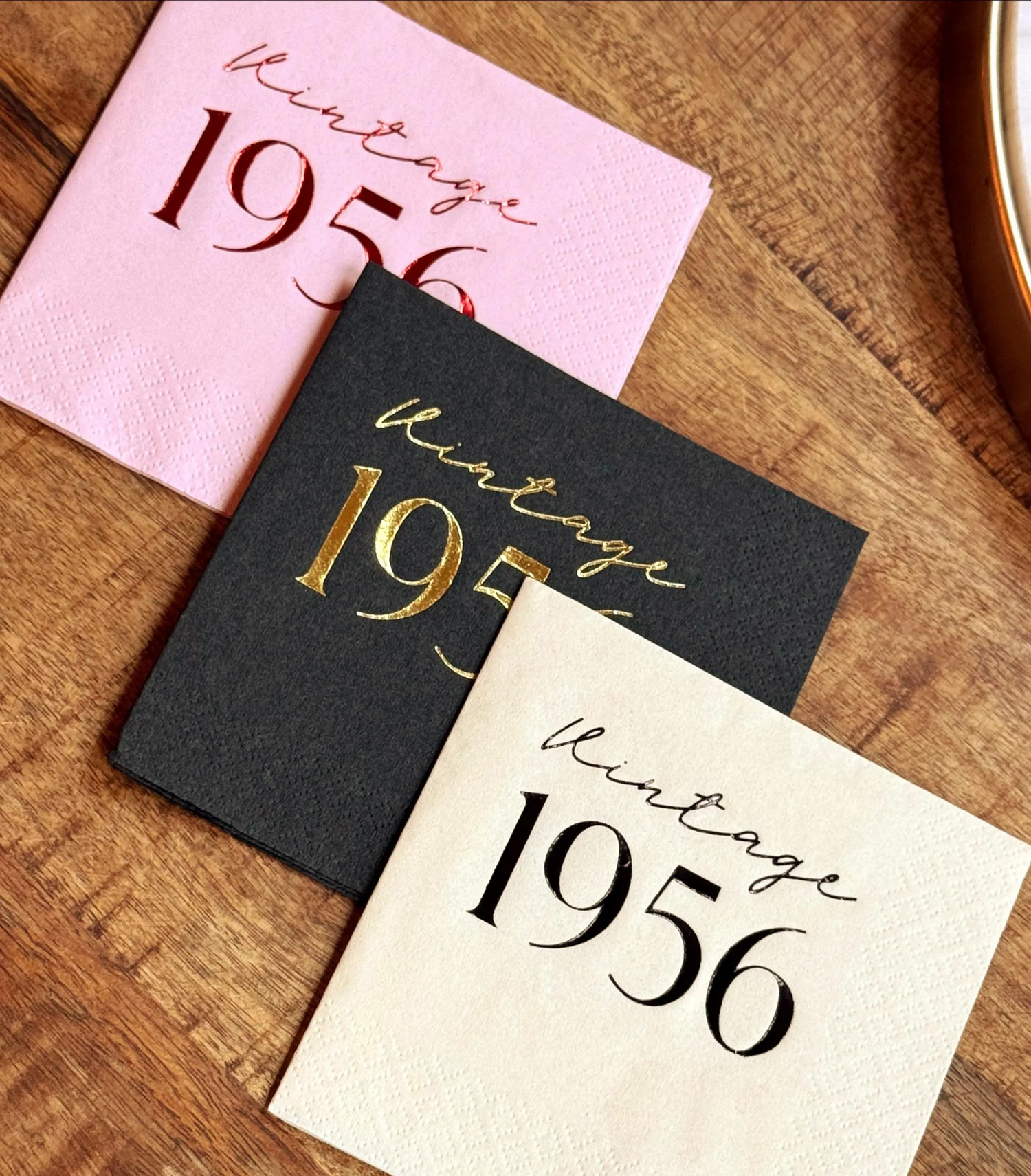 Three cocktail napkins with 'Vintage 1956' text on a wooden surface