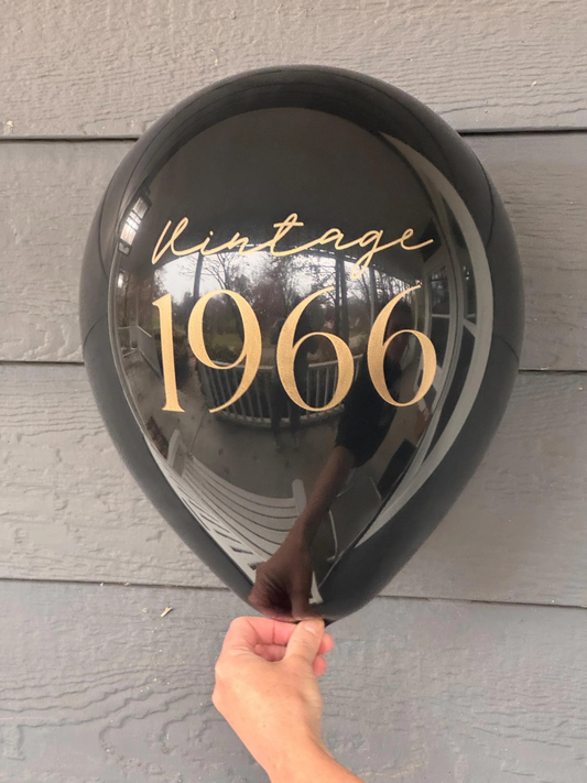 Black balloon with 'Vintage 1966' text held against a wooden surface