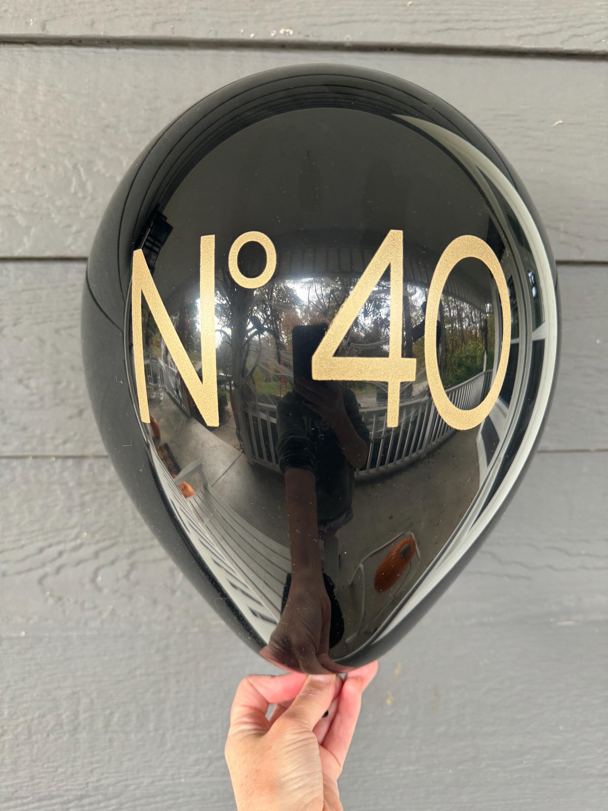 Black No 40 birthday balloon with gold lettering against gray horizontal siding.
