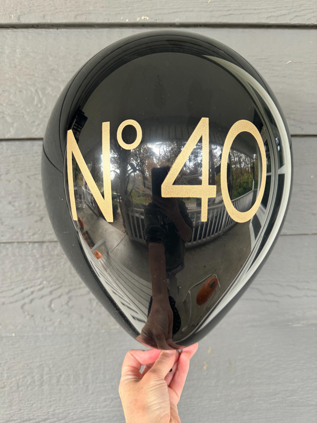 Hand holding a glossy black No 40 latex birthday balloon with gold lettering.