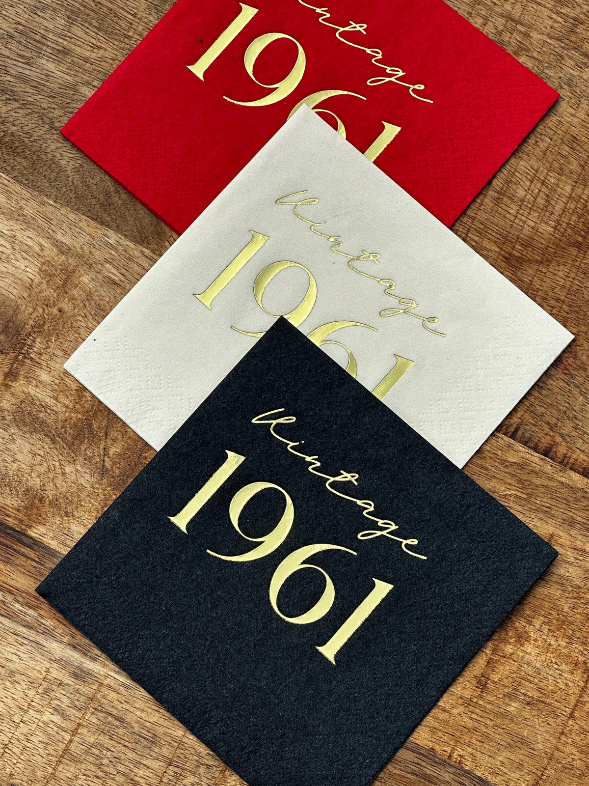 Three layered square cocktail napkins in red, white, and black, each stamped with metallic text reading Vintage 1961.