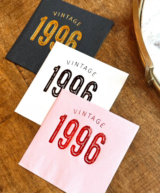 Three napkins with 'Vintage 1996' text in different colors on a wooden surface.