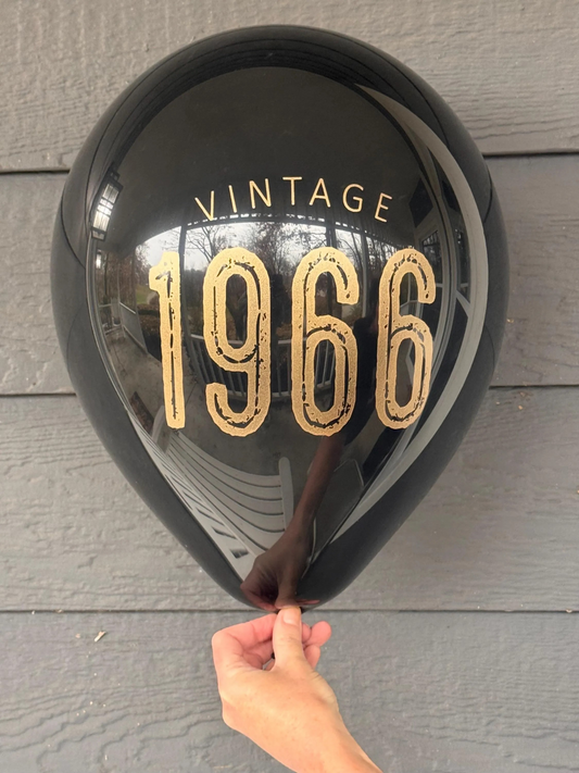 Black balloon with 'Vintage 1966' text held by a hand against a wooden background